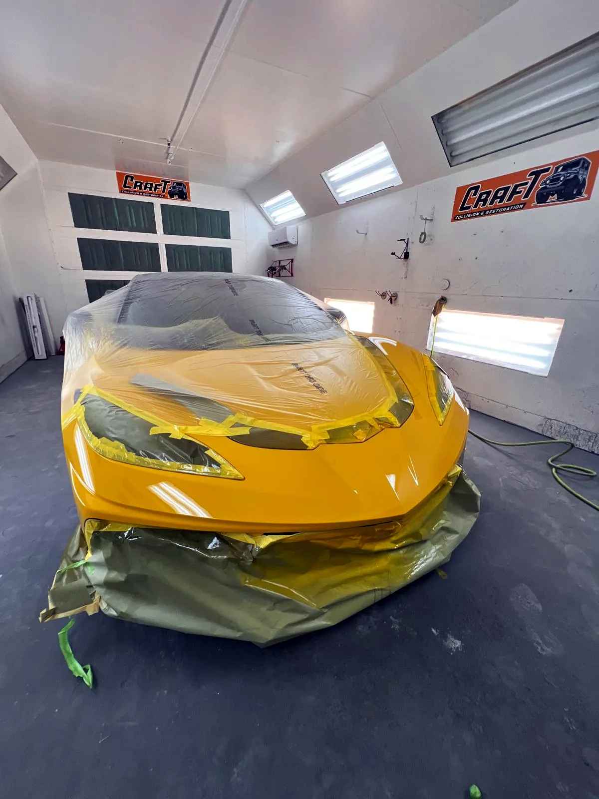 Yellow Corvette C8 masked with paper and tape inside the paint booth
