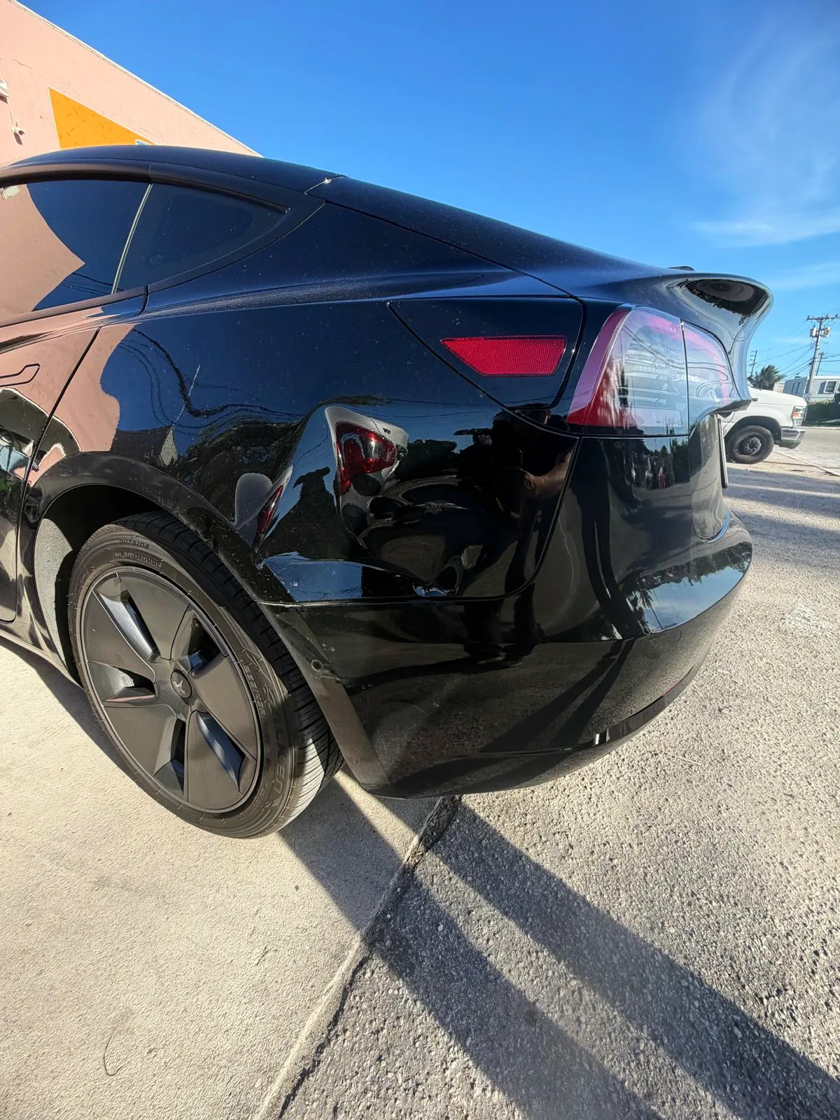 Dent in the rear quarter panel of a black Tesla Model 3 before repair