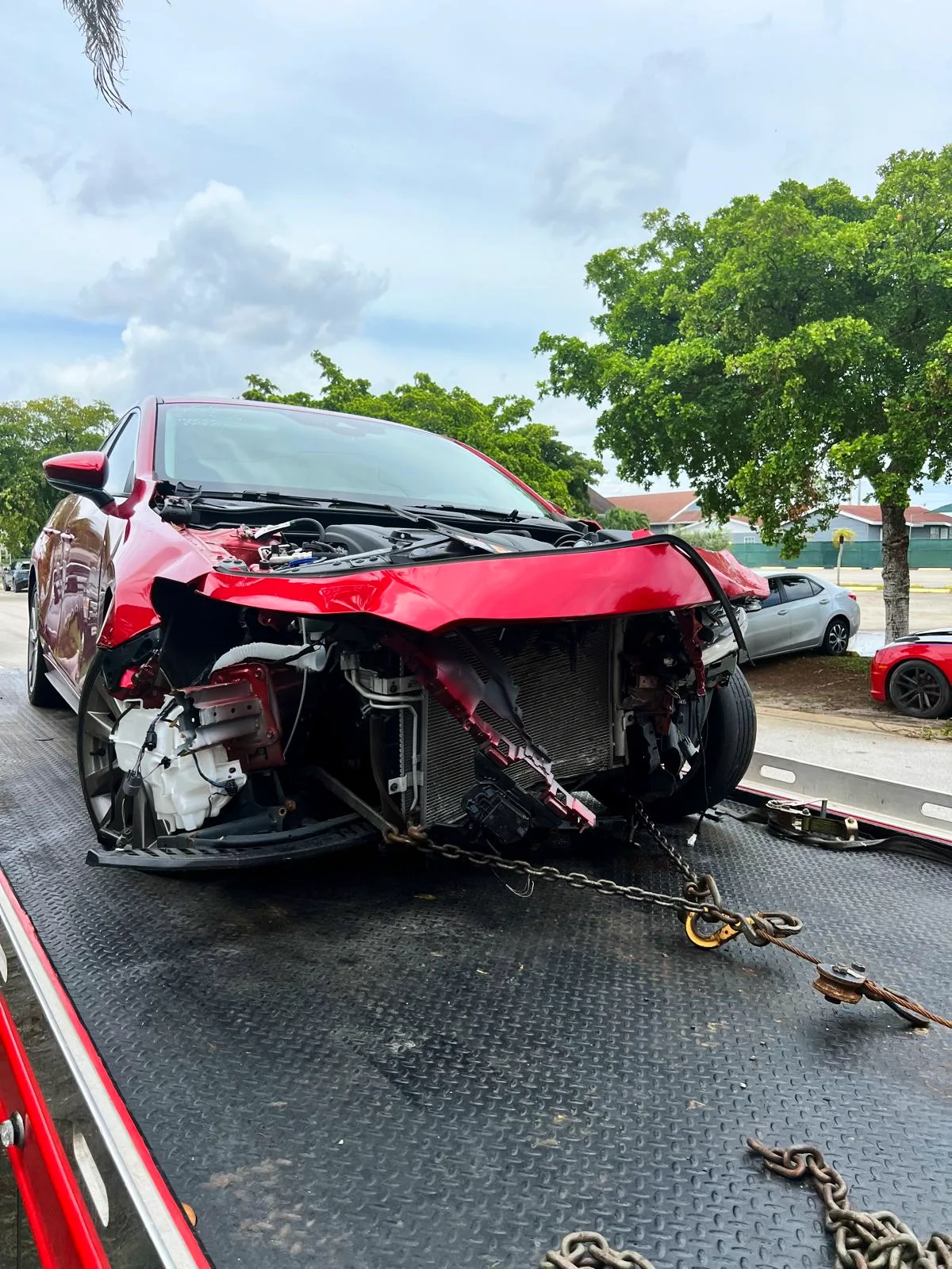 Red sedan with heavy front-end collision damage arriving on a flatbed tow truck